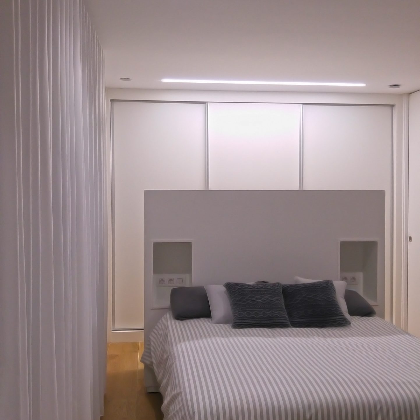 Dormitorio pequeño con cortinas, cabezal, armario, techo y paredes todo en blanco, para que parezca más grande el dormitorio